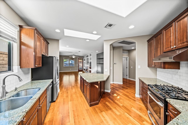 kitchen with a skylight, light stone countertops, sink, and appliances with stainless steel finishes