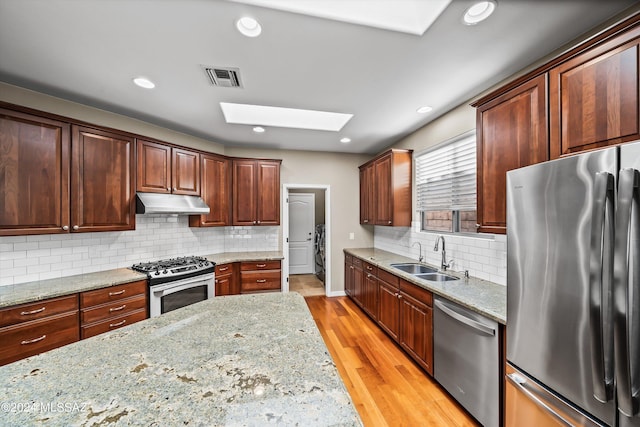 kitchen featuring sink, a skylight, light stone countertops, appliances with stainless steel finishes, and light hardwood / wood-style floors