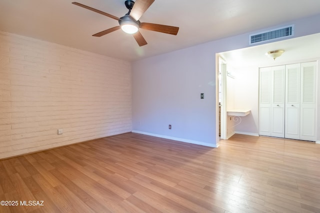 unfurnished bedroom featuring ceiling fan, light wood-type flooring, brick wall, and a closet