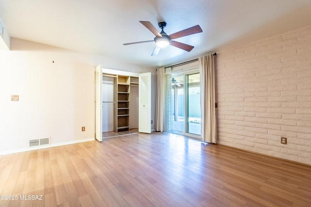 spare room with ceiling fan, light hardwood / wood-style flooring, and brick wall