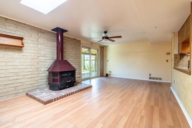 unfurnished living room with a skylight, a wood stove, ceiling fan, and light hardwood / wood-style floors