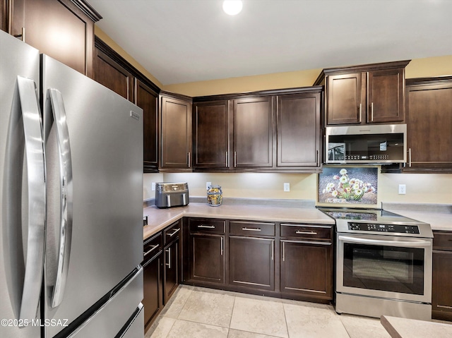 kitchen with dark brown cabinets, light tile patterned floors, and stainless steel appliances