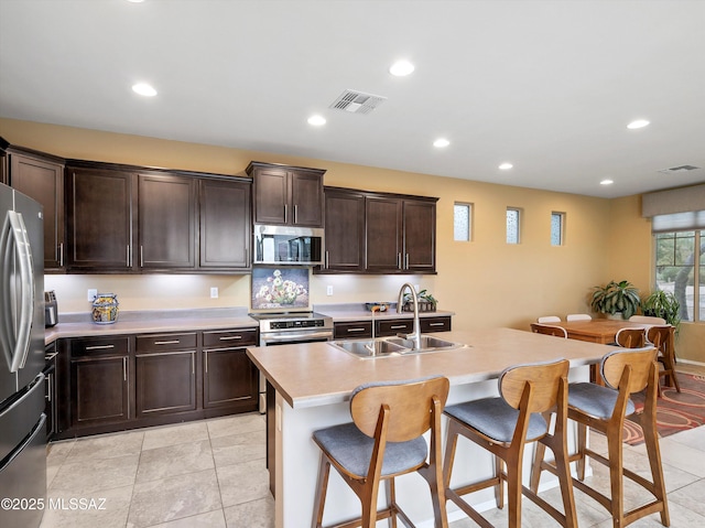 kitchen featuring appliances with stainless steel finishes, a breakfast bar, sink, light tile patterned floors, and an island with sink