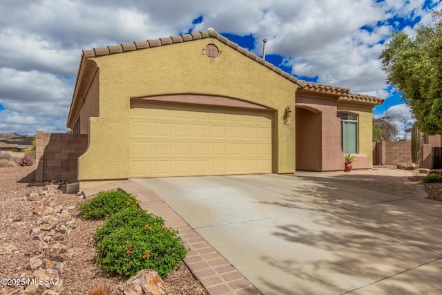 mediterranean / spanish home with a garage, a tiled roof, concrete driveway, stucco siding, and fence