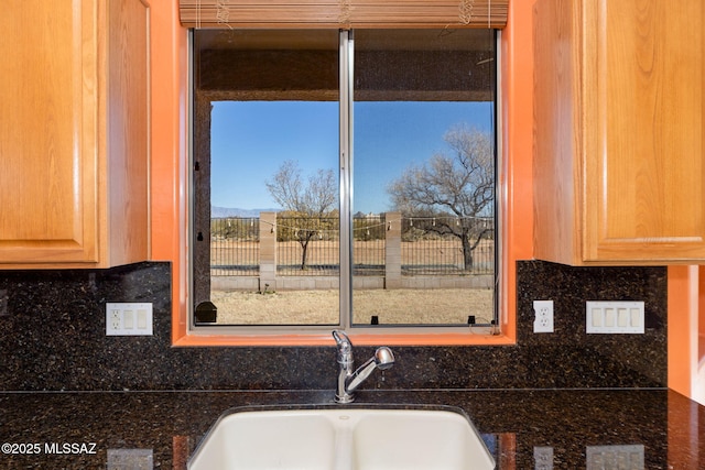 kitchen with tasteful backsplash, light brown cabinets, dark stone counters, and a sink