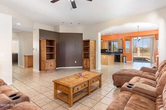 living room with built in shelves, ceiling fan with notable chandelier, arched walkways, and light tile patterned floors