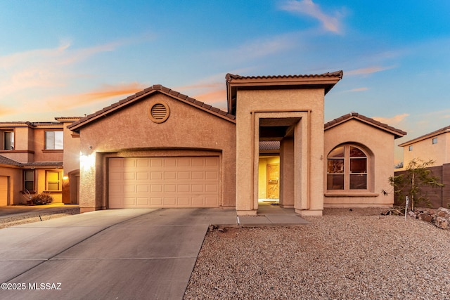 mediterranean / spanish home featuring a garage, driveway, a tile roof, and stucco siding