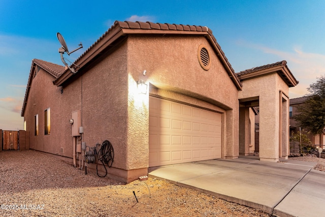 view of side of property featuring a garage, a tile roof, fence, concrete driveway, and stucco siding