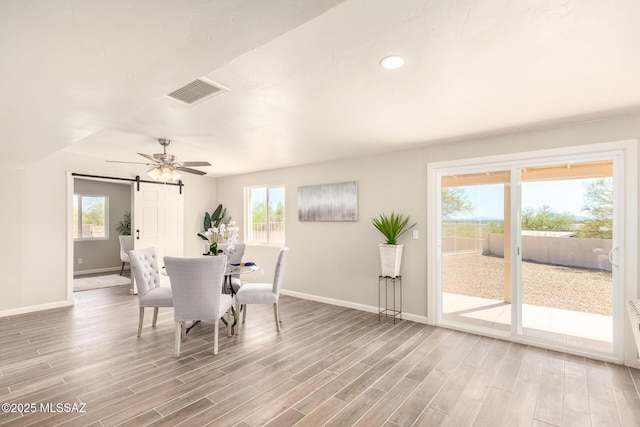 dining space featuring wood-type flooring, a barn door, and ceiling fan