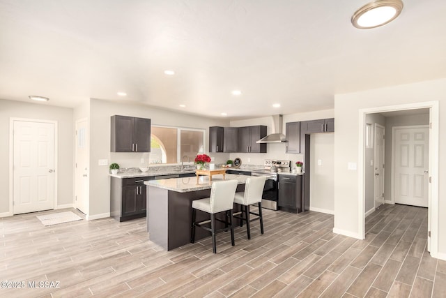 kitchen with wall chimney exhaust hood, a breakfast bar, stainless steel range with electric cooktop, a kitchen island, and light stone countertops