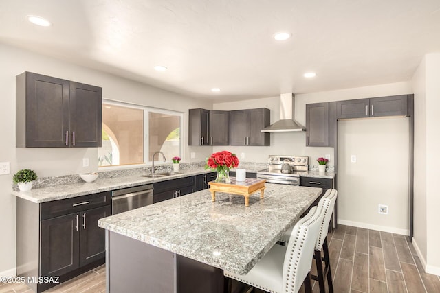 kitchen with wall chimney exhaust hood, sink, a center island, stainless steel appliances, and light stone countertops