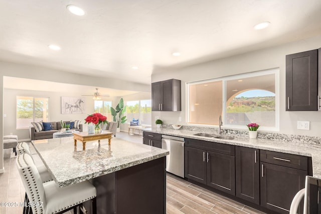 kitchen with sink, light stone counters, dark brown cabinets, stainless steel dishwasher, and a kitchen breakfast bar