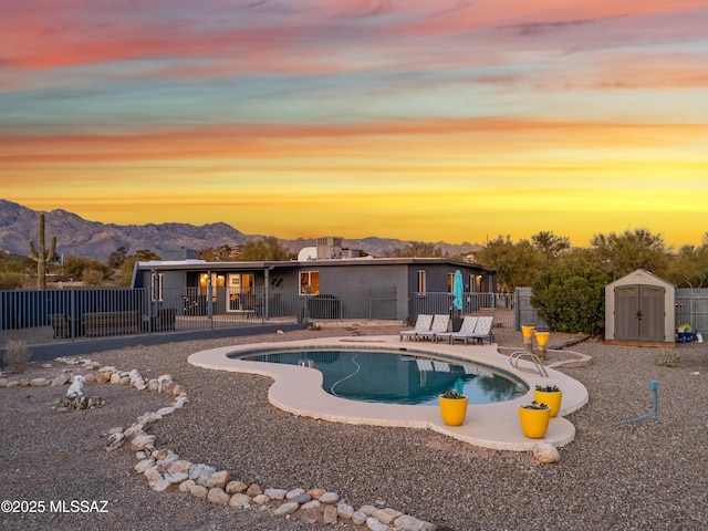 pool at dusk with a storage unit, a mountain view, and a patio