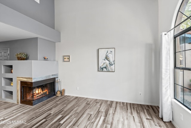 unfurnished living room with a towering ceiling, baseboards, wood finished floors, and a multi sided fireplace