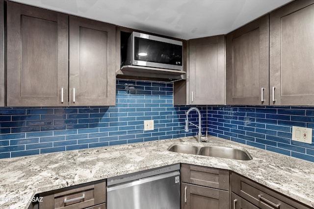 kitchen featuring stainless steel appliances, light stone counters, a sink, and decorative backsplash