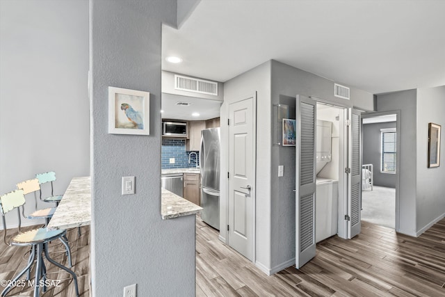 kitchen featuring light hardwood / wood-style floors, appliances with stainless steel finishes, tasteful backsplash, a breakfast bar, and stacked washing maching and dryer