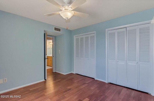 unfurnished bedroom featuring ceiling fan, wood-type flooring, and multiple closets