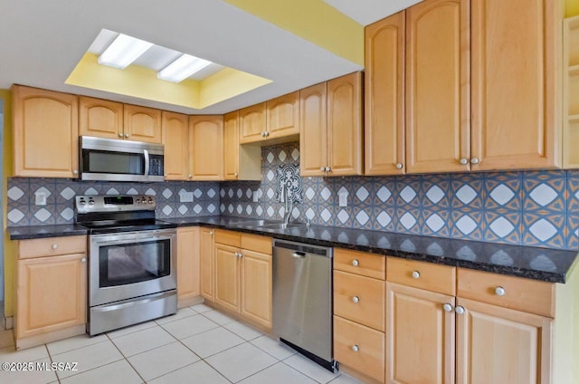 kitchen featuring sink, stainless steel appliances, backsplash, dark stone counters, and light tile patterned floors