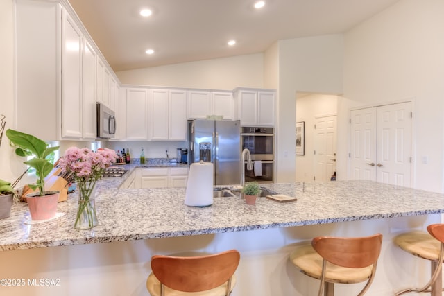 kitchen featuring a kitchen breakfast bar, white cabinetry, appliances with stainless steel finishes, and lofted ceiling