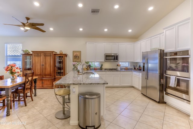 kitchen with ceiling fan, appliances with stainless steel finishes, an island with sink, white cabinets, and light stone counters