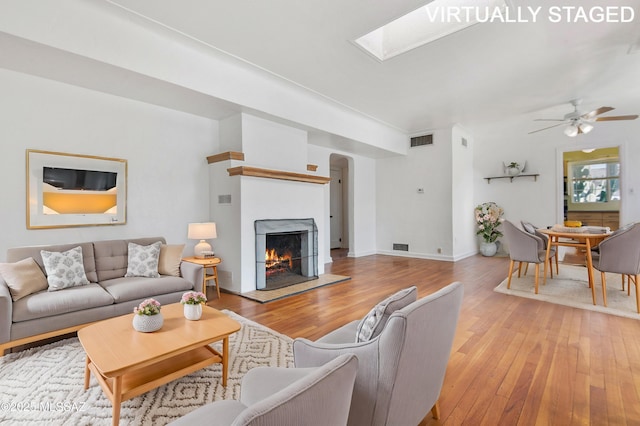 living room featuring a skylight, light hardwood / wood-style flooring, and ceiling fan