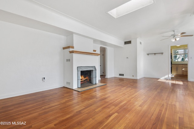 unfurnished living room featuring ceiling fan, a skylight, and hardwood / wood-style floors