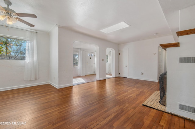 unfurnished living room with hardwood / wood-style flooring, ceiling fan, and a skylight