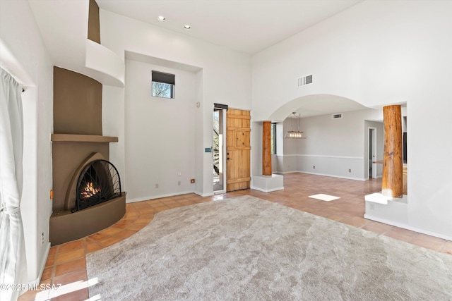 unfurnished living room featuring light tile patterned floors, a high ceiling, and decorative columns