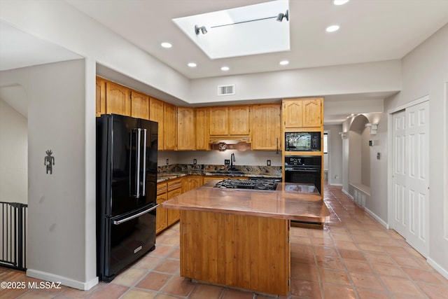 kitchen featuring a skylight, light tile patterned flooring, a kitchen island, black appliances, and sink