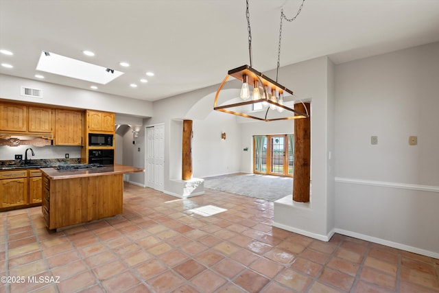 kitchen with a center island, black appliances, a skylight, sink, and hanging light fixtures