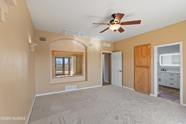 unfurnished bedroom with ensuite bath, light colored carpet, ceiling fan, and rail lighting