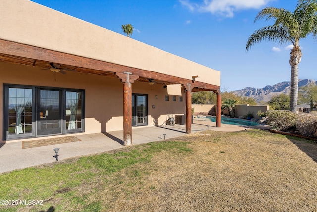 rear view of property with a mountain view, a lawn, ceiling fan, a fenced in pool, and a patio