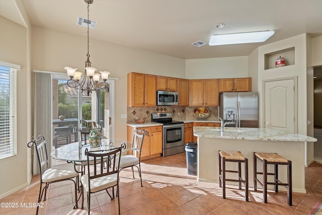 kitchen with pendant lighting, a kitchen island with sink, tasteful backsplash, a notable chandelier, and stainless steel appliances