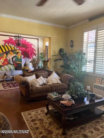living room featuring ceiling fan, radiator heating unit, wood-type flooring, a textured ceiling, and ornamental molding