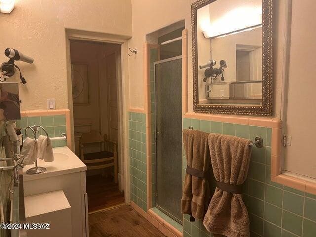 bathroom featuring toilet, vanity, a shower with shower door, tile walls, and hardwood / wood-style flooring
