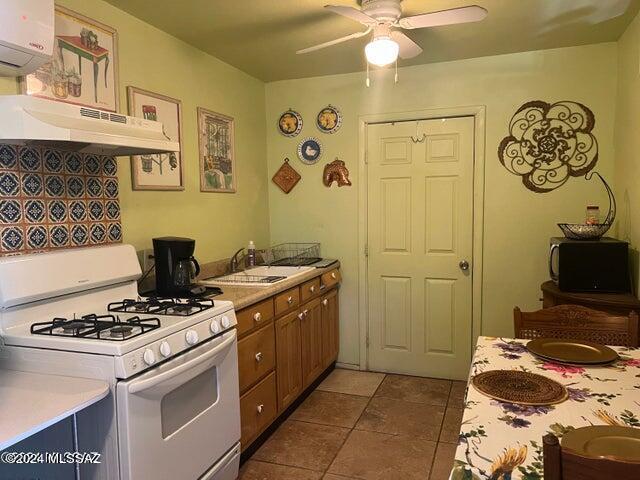 kitchen featuring a wall mounted air conditioner, sink, white gas range oven, ceiling fan, and dark tile patterned floors