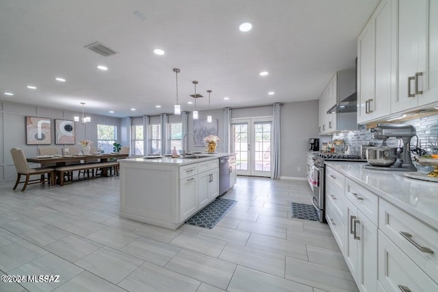 kitchen featuring hanging light fixtures, appliances with stainless steel finishes, white cabinetry, and a center island with sink