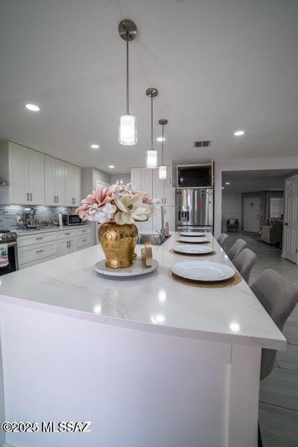 kitchen featuring white cabinetry, stainless steel fridge, backsplash, a kitchen breakfast bar, and pendant lighting