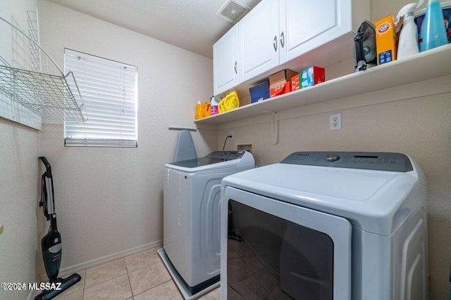 clothes washing area featuring light tile patterned floors, washing machine and clothes dryer, and cabinets