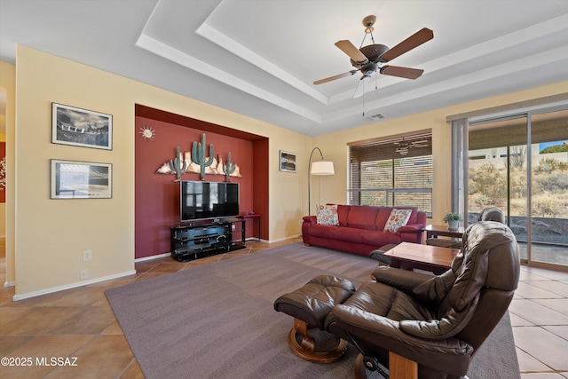 tiled living room with a tray ceiling and ceiling fan