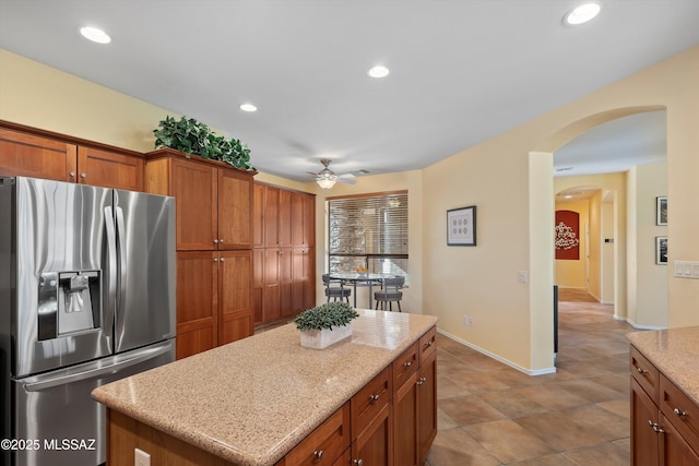 kitchen featuring light stone countertops, stainless steel fridge, a center island, and ceiling fan