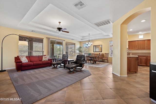 living room featuring ceiling fan with notable chandelier, light tile patterned floors, sink, and a tray ceiling