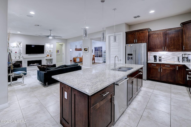 kitchen with sink, dark brown cabinets, stainless steel appliances, light stone countertops, and a kitchen island with sink