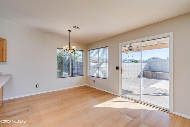 unfurnished dining area with ceiling fan with notable chandelier, hardwood / wood-style flooring, and plenty of natural light