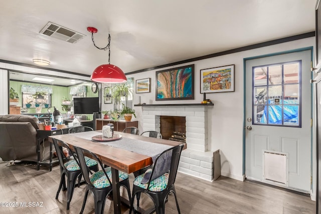 dining area with a brick fireplace, plenty of natural light, wood-type flooring, and crown molding