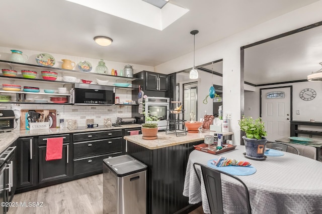 kitchen with light stone countertops, appliances with stainless steel finishes, light hardwood / wood-style floors, hanging light fixtures, and backsplash