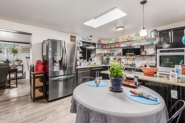 kitchen featuring a skylight, light hardwood / wood-style floors, stainless steel appliances, decorative light fixtures, and light stone countertops