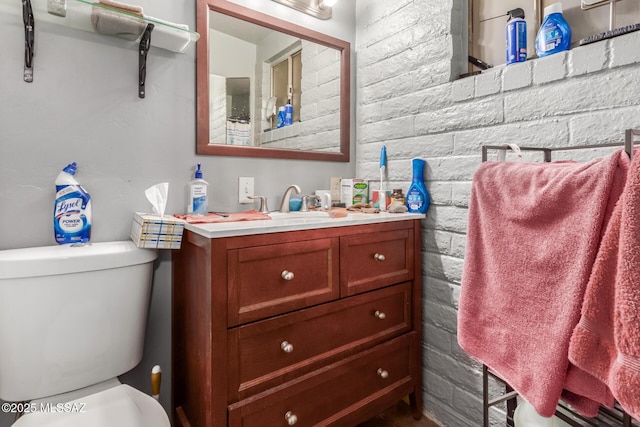 bathroom with toilet, vanity, and brick wall