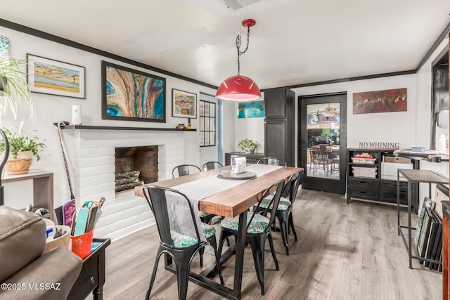 dining space featuring light wood-type flooring, a brick fireplace, and ornamental molding