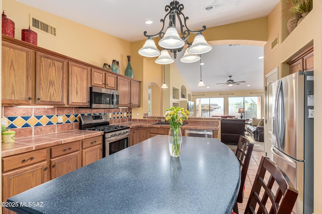 kitchen with pendant lighting, backsplash, ceiling fan with notable chandelier, a towering ceiling, and appliances with stainless steel finishes